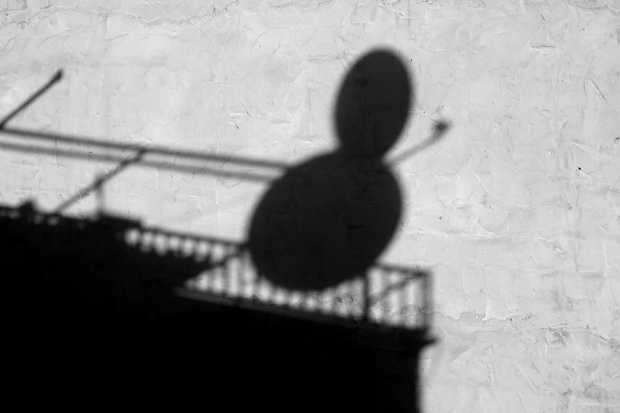 Shadow of a balcony and a satellite dish on a wall, in black and white