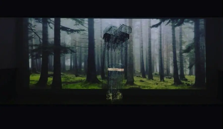 Wire-mesh house suspended in front of a projected forest, installation view