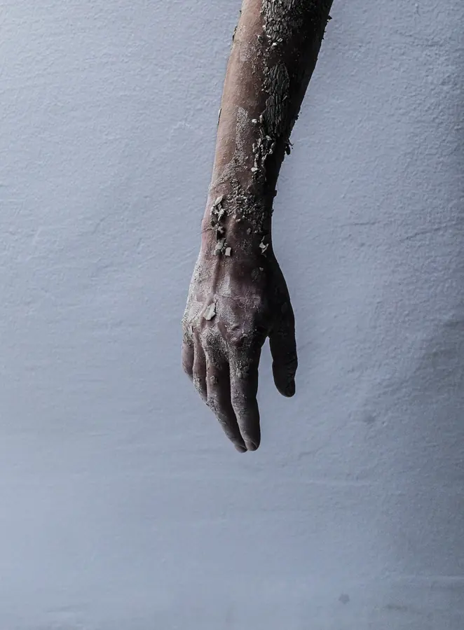 Hand covered in dried clay against a pale wall