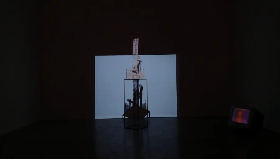 Small sculpture in front of a lit screen in a dark exhibition room